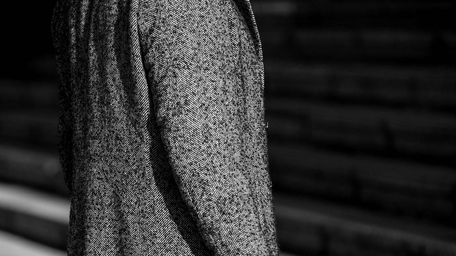 The sleeve of a herringbone wool overcoat, seen close in black and white